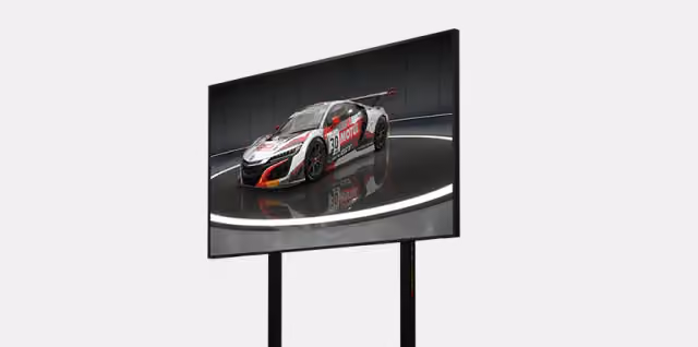 Duży monitor z wyświetlaną grafiką auta wyścigowego zamontowany na czarnym stojaku Next Level Racing